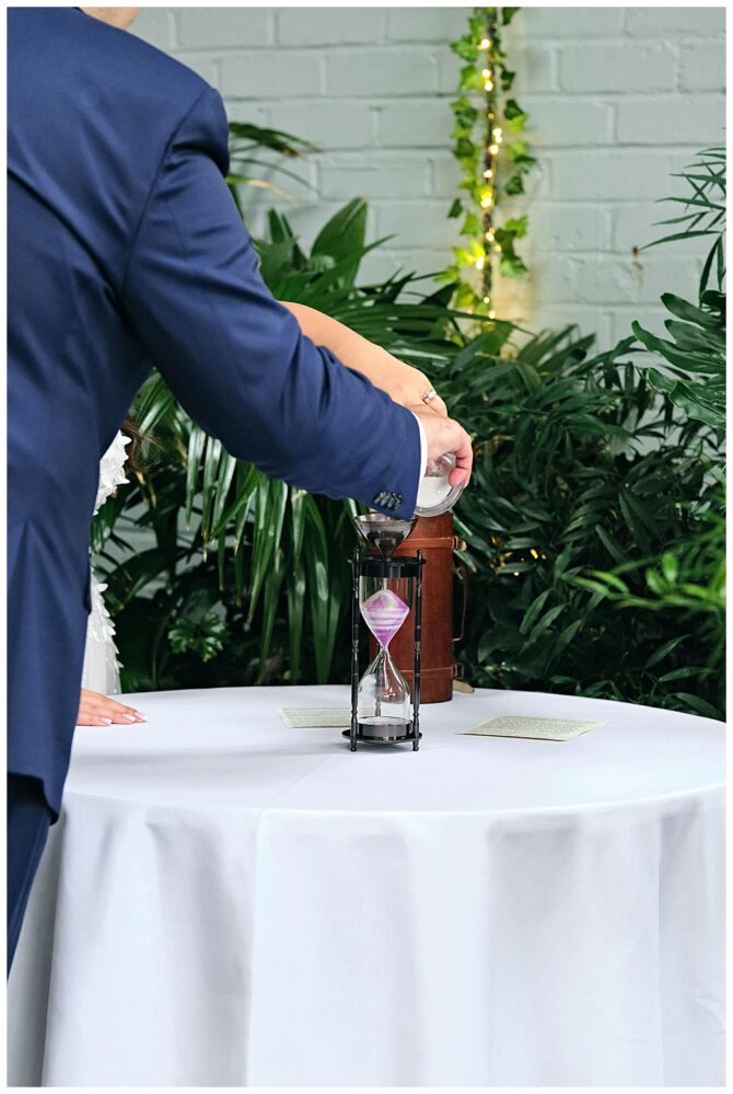 Couple pouring sand into an hourglass at wedding.
