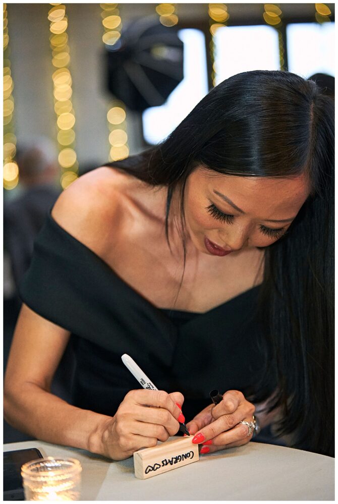Woman writing on wooden block at event table.
