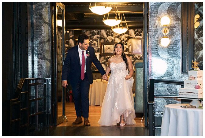 Wedding couple entering reception venue holding hands.