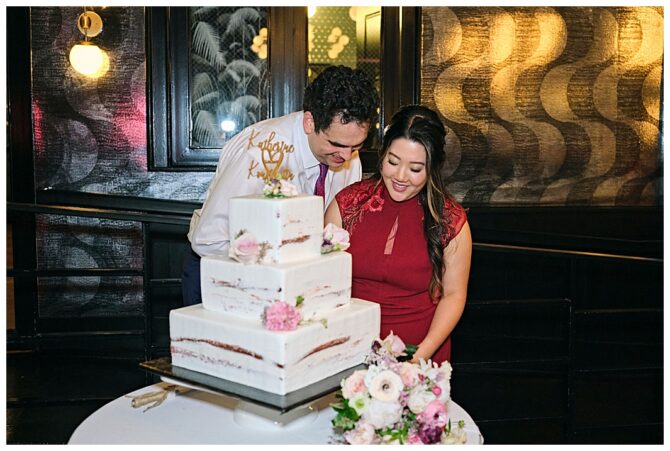 Couple cutting a tiered wedding cake together.