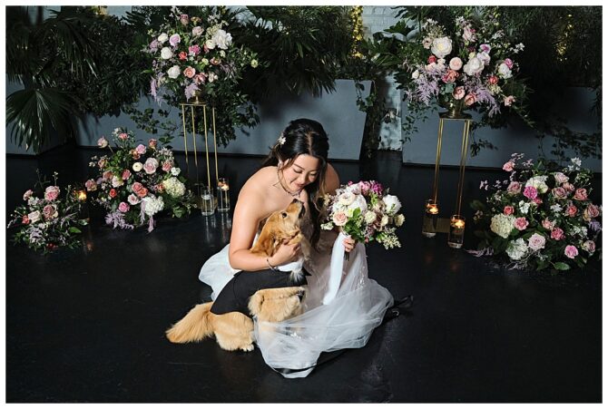 Bride cuddling dog among floral arrangements