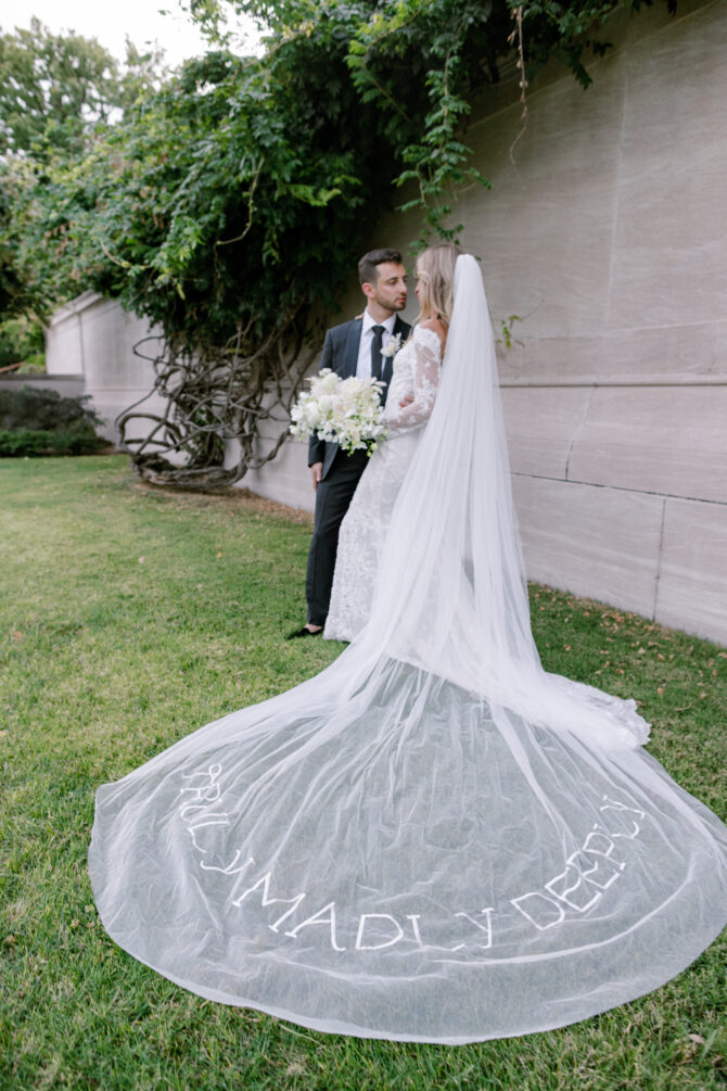 Bride and groom with embroidered veil outdoors.