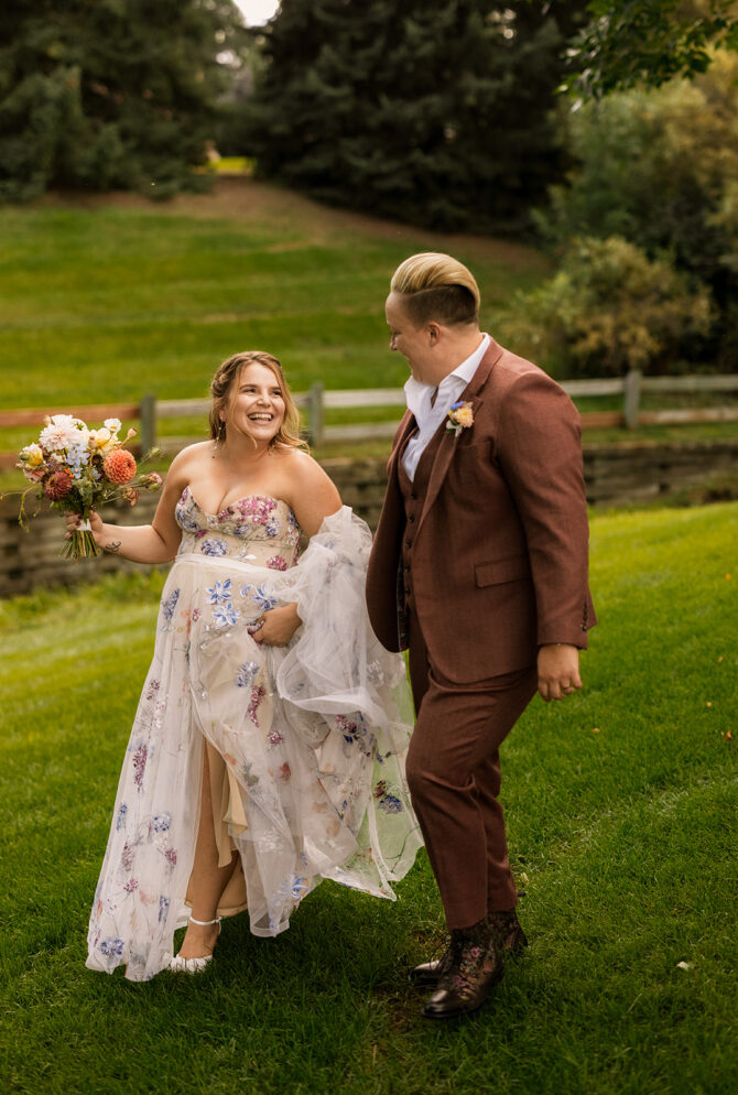 Bride and groom walking on grass, smiling.