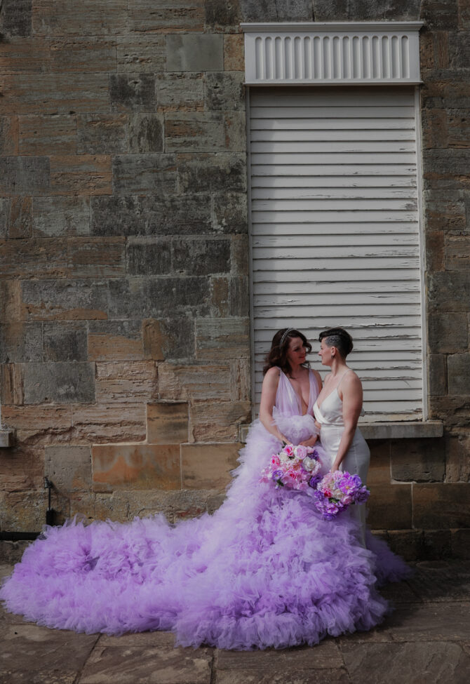 Two women in wedding dresses with floral bouquets.