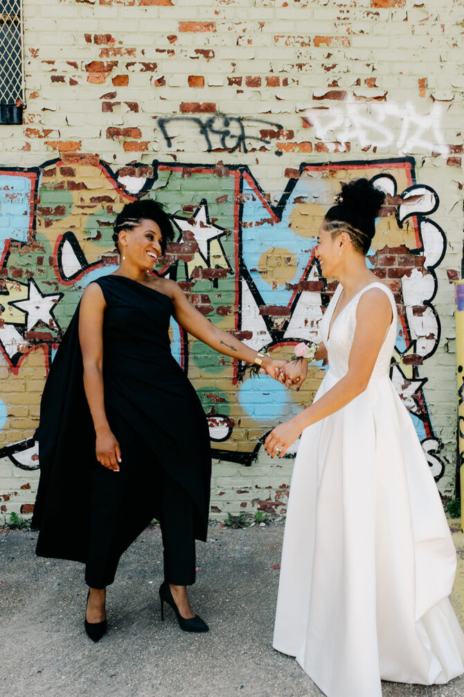 Two women celebrating in front of graffiti wall.