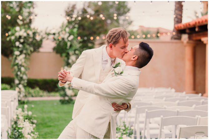 Groom kissing groom in outdoor wedding ceremony.
