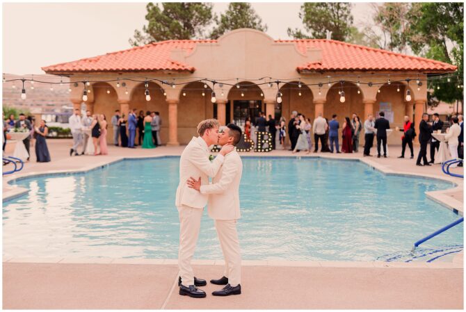 Grooms kissing by the pool at wedding reception.
