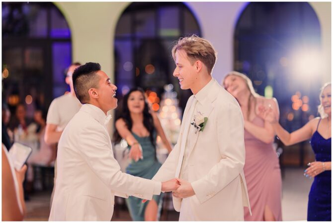 Two grooms happily dance at wedding reception.