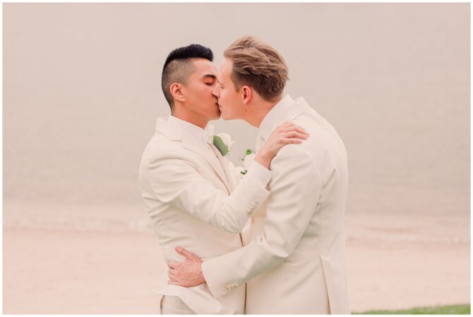 Two grooms kissing by the beach.