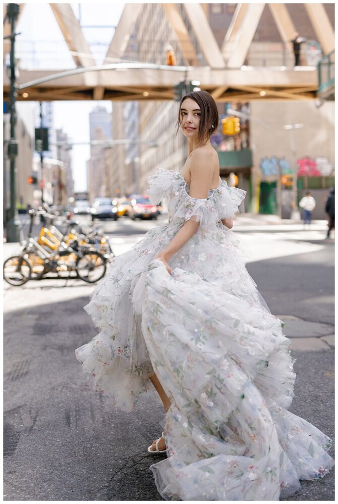 Woman in floral dress twirling on city street.