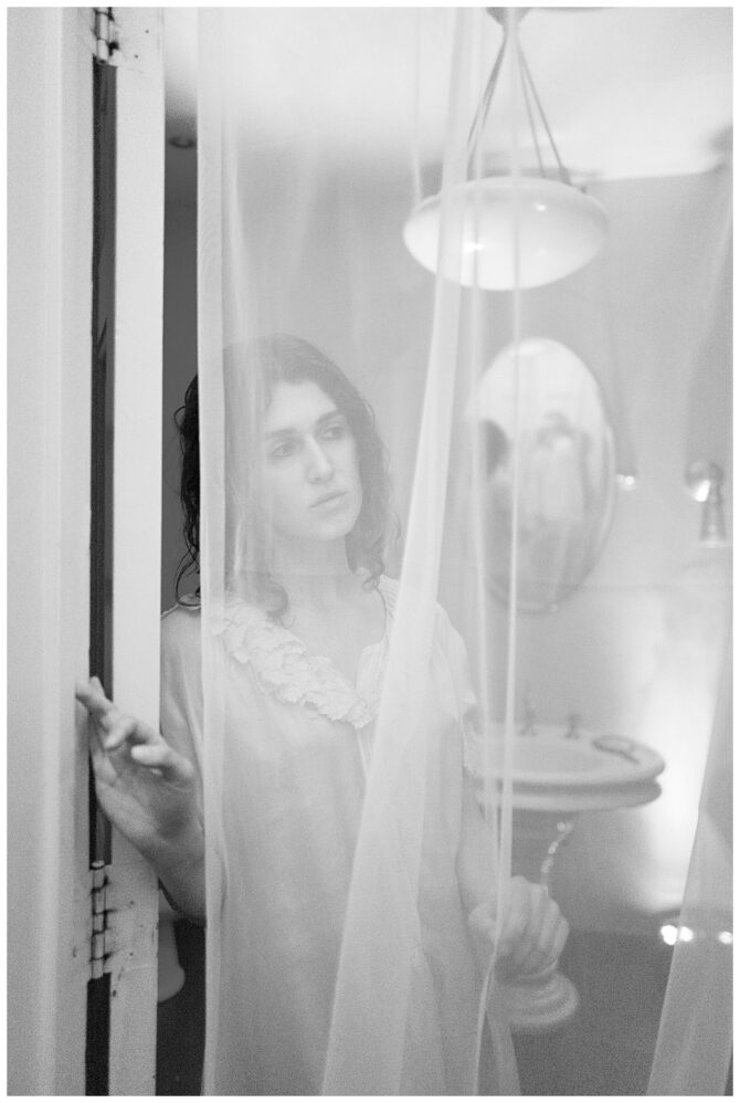 Woman behind sheer curtain in dimly lit room.