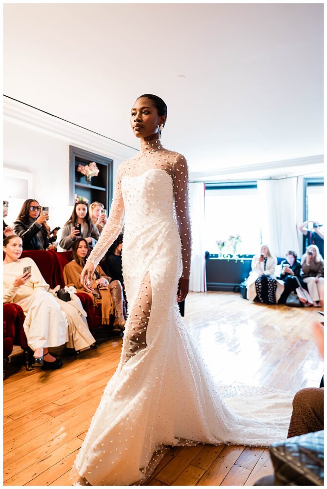 Model walking runway in elegant white gown.
