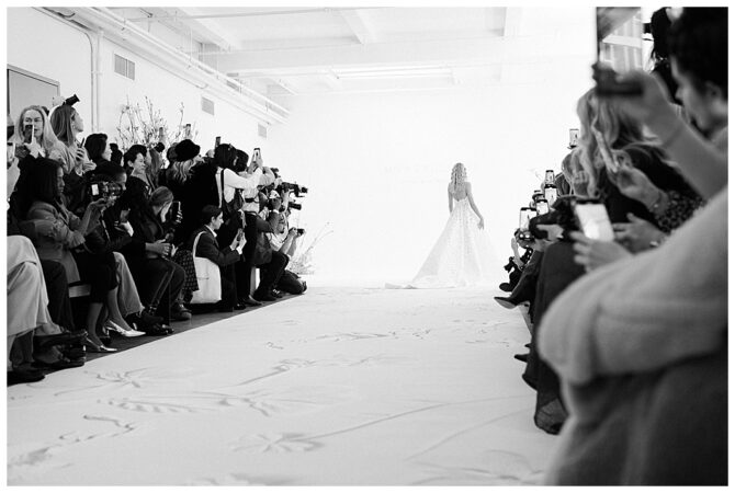 Bride walks runway, photographers capturing event.